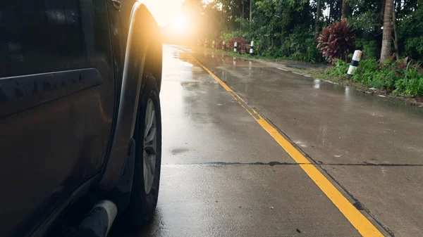 Front view of a car with a focus on the wheels of a car running on a wet concrete road. Rain-wet rural forest environment.