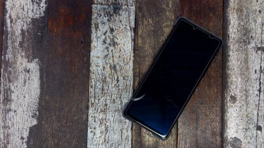 Parlak, siyah çerçeveli akıllı telefon manzarası. Ahşap bir zemine yerleştirilmiş çeşitli güzellikte..