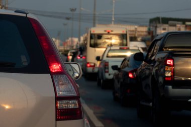 Beyaz arabanın arka tarafında fren lambası açık. Şehirdeki asfalt yolda trafik sıkışık. Akşamları trafik sıkışıklığı.