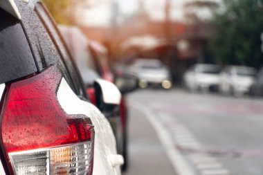 Asfalt yolda beyaz araba durağı lüksü. Islak yağmur damlasıyla arabada. Aydınlık bir dönemde taşralarda seyahat etmek. Birçok araba yol kenarında bir kuyruğa park edilmiştir.. 