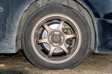 Otoparktaki siyah bir arabanın tekerine yakın çekim. Geceleri toprak yol çevresi.