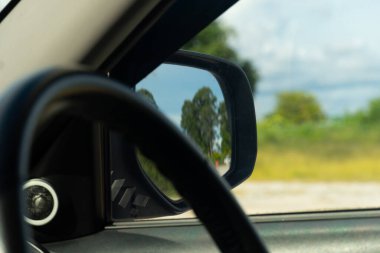 Arabanın ayna görüntüsünü kapat. Gökyüzünün altındaki yeşil çimlerin manzarasıyla. Arabanın içindeki bulanık direksiyonun yazı tipi.