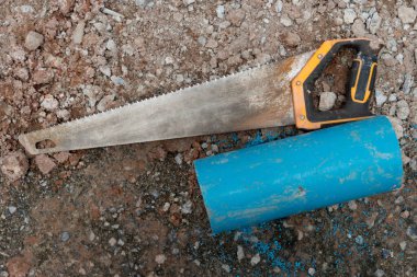 Tek elle yapılmış çok amaçlı testerenin üstünde, sapı olan. Ve yanında 8 santimlik bir su borusu kesilmiş. Çakıl toprağı.