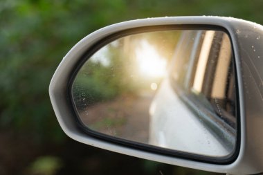 Güneş ışığı olan beyaz arabanın aynasına bak. yeşil ağacın arkaplanı.