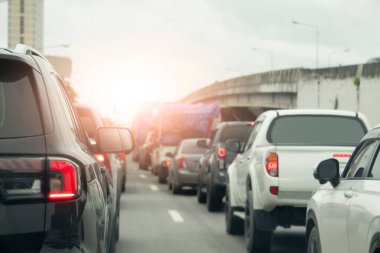 Arabanın arka tarafında dur ve asfalt yolundaki fren lambasında koş. Kavşaklardaki trafik sıkışıklığı sırasında bir sürü araba parkı ve kuyruk var. Çimento köprüsü olan arabanın yanında. Parlak gökyüzünün altında.