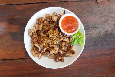 Tayland usulü kızarmış domuz sarımsaklı. Biraz baharatlı sosla servis edilmiş. Beyaz bir tabağa ve tahta bir yüzeye yerleştir..