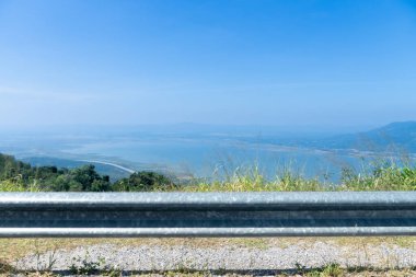 Yolun muhafız merceğinin yatay görüntüsü. Yeşil kenarda büyüyen çakıl ve çimlerle. Lam Takhong Reservoir ve uzak bulanık dağ aralığının görüntüsü.
