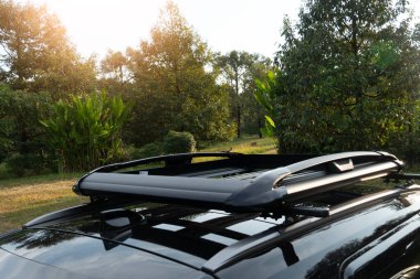 Siyah bir arabanın tepesinde seyahat etmek için bir bagaj rafı bulunur. Kamp alanındaki yeşil çimenlerin ve Durian bahçesinin arka planı