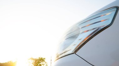 Modern araba farlarını kapat. Farlar parlak ve fütüristik. Parlak, güneşli bir arka planda, arabanın yüksek teknolojili özelliklerini ve lüks görünümünü ön plana çıkarıyor..