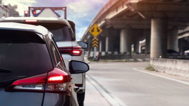 Arka taraftaki siyah renkli araçlar yolculuğun amacına doğru ilerliyor. Fren lambasını yakarak. Gündüz trafiği yoğun. Kenarda bir köprü var..