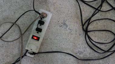 Beton zeminde duran eski bir elektrik prizi. Üç priz de çalışıyor. Kablolar birbirine bağlıdır ve estetik açıdan hoş değildir..