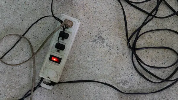 Beton zeminde duran eski bir elektrik prizi. Üç priz de çalışıyor. Kablolar birbirine bağlıdır ve estetik açıdan hoş değildir..