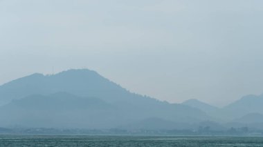 Okyanusun manzarası. Büyük ada ya da dağın altındaki ormanlık bir sahil köyü. Ve karanlık gökyüzü.