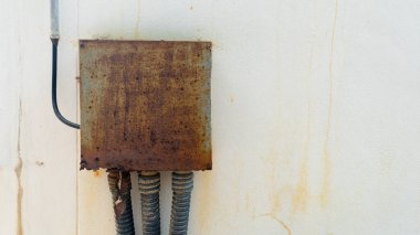 Paslı kare metal kutu yıpranmış beyaz bir duvara monte edildi. Güç ve sinyal kabloları metal bir kutunun içindeki bir bağlantıya bağlıdır. Siyah plastik esnek bir tüple kaplıydı. Çimento duvarına kur.