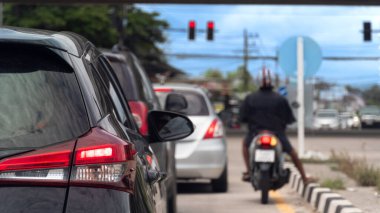 Arabanın arka tarafı siyah arabanın stop lambasını kapat. Arabalar kırmızı ışıkta motosikletle sıraya girdiler. Yolun ortasında üstgeçidin önü gölgedir. Mavi gökyüzünün altında.