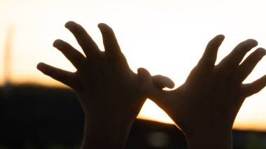 Güneşe doğru yükselen iki elli siluet bir kuş ya da kelebek şekli oluşturuyor. Sıcak arka plan huzurlu ve umut verici bir hava yaratıyor. Özgürlük hayalleri ve çocukluk teması için fikirler.