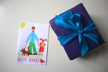 Çocuk tarafından çizilmiş bir baba için kartpostal fotoğrafı. Mavi renkli ve fiyonklu bir hediye. Beyaz arka plan. Kalemle çizim yapmak. Babam kız ve köpekle tasvir ediliyor. Dondurma yiyen kız. En İyi Baba 'ya ithaf..