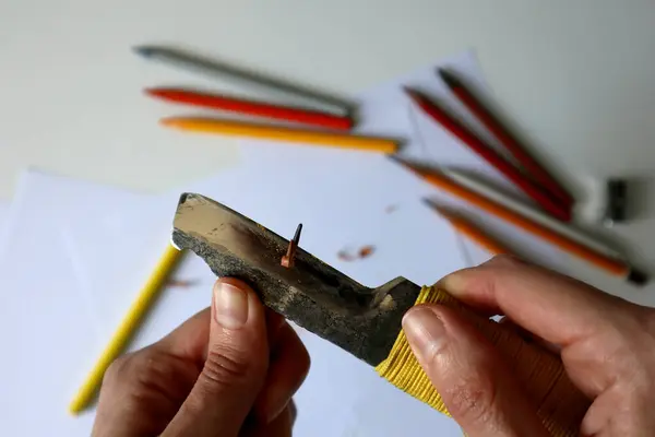 Kâtip bıçağıyla kalemleri açarken çekilmiş bir fotoğraf. İnsan eli. Metal bıçak. Arka planda beyaz kağıtlar ve renkli kalemler var. Yaratıcılık, çizim, sanat, sanatçı.