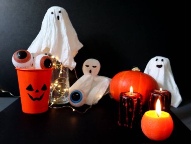 Set of various elements for Halloween. Jack o lantern glass is filled with eyes. Orange and black candles with red drops. Pumpkin. Toy little ghosts with different facial expressions. Black background clipart