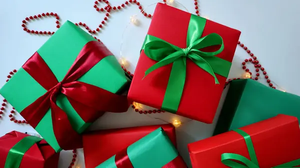 Beyaz arka planda hediyeler. Geleneksel Noel kırmızı ve yeşil renkler. Farklı boyutlarda kutular. Kurdele ve fiyonklarla bağlanmış. Kırmızı boncuklardan oluşan bir çelenk ve sarı bir çelenk. Fotoğraf..