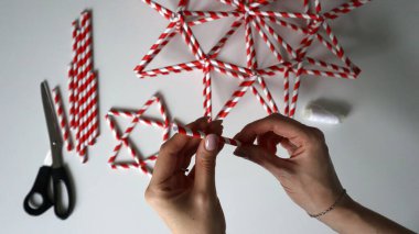 El yapımı. Kadın eli iplikle iğneyi tutuyor. Kokteyller için kağıt tüplerden Noel yıldızları yaratma sürecinde. Kırmızı, beyaz çizgili tüpler. Makas, beyaz iplik. Beyaz arka plan. Fotoğraf.