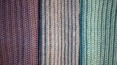 Arka plan örülmüş kumaştan yapılmış üç dikey parçaya bölünmüş. Çeşitli dokular ve renkler. Turkuaz, gri, mor. Sıcak kıyafetler, örgü, hobi, el yapımı..