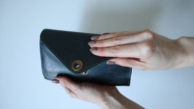 Kadın elleri cüzdanı, el çantasını açar. Beyaz arka plan. Beyaz eller, açık kahverengi tırnak. Koyu mavi, turkuaz cüzdan. Dikdörtgen şeklinde, avuç içi büyüklüğünde. Çılgın at derisi. Altın renkli toka. Fotoğraf..