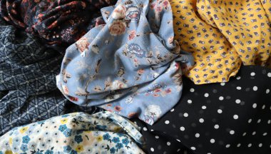 Baskılı kumaş fotoğrafları. Farklı renkler ve desenler. Kaotik bir şekilde yerleştirilmiş, farklı şekillerde buruşmuş. Çiçek izleri, puantiyeler, süslemeler. Mavi, siyah, sarı, kahverengi, beyaz, vs. Giyinme.