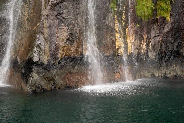 Milford Sound, NZ 'de nefes kesici bir şelale. Kayalık kayalıkların üzerinde güçlü bir şelale, berrak bir havuz oluşturuyor. Bereketli çevre ve değişen mevsimler canlı renkleri artırır..