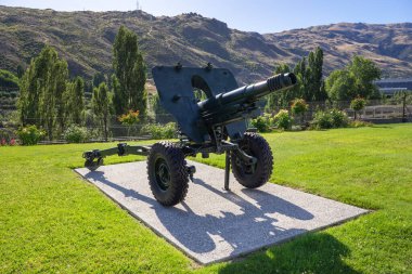 Clyde, Yeni Zelanda - 9 Mayıs 2023. Tarihi bir L5 Pack Howitzer topu yemyeşil bir platformun üzerinde gururla duruyor, bereketli doğayla çevrili. Koyu yeşil gövdesi ve öne çıkan tekerlekleri dikkat çekiyor.