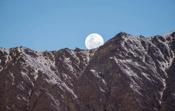 Aydınlık ay gökyüzüne hükmediyor, alttaki engebeli bir dağa ışık tutuyor. Bu göksel sahne dramatik manzara üzerinde ay doğuşunun dinginliğini yakalar. Queenstown, Yeni Zelanda