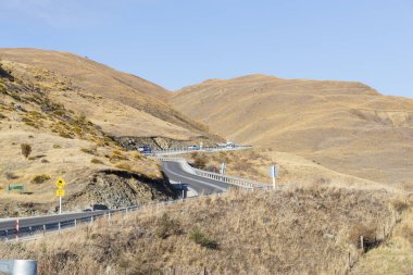 Pisa Koruma Alanı, Yeni Zelanda 'nın dağlık tepelerinde arabalar, yol işaretleri ve gözlem noktalarıyla dolambaçlı yol. Tepeleri kaplayan alp bitkilerinin olduğu resim gibi bir bahar manzarası..