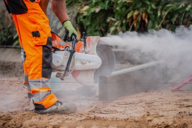 Elektrikli testereyle çalışan koruyucu kıyafetli bir inşaat işçisi.
