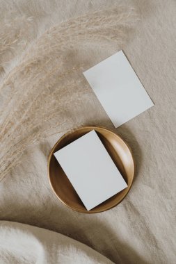 Pirinç tabakta boş kağıt kağıtlar, nötr bej bezde pampa otları buruşuk keten kumaşlar. İş planı. Üst görünüm, düz uzanan minimalist estetik lüks bohem ticari markalaşma kavramı
