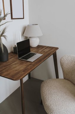Masada dizüstü bilgisayar, lamba ve rahat sandalye var. Estetik ev ofis çalışma alanı iç tasarımı. Online alışveriş, çevrimiçi mağaza, sosyal medya, blog markalaşması