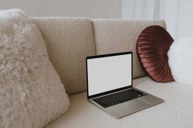 Yastıklı rahat bir kanepede boş ekranlı dizüstü bilgisayar. Taklit alanı olan estetik şablon. Çevrimiçi mağaza, blog, sosyal medya, web sitesi markalaşması. Çevrimiçi alışveriş kavramı