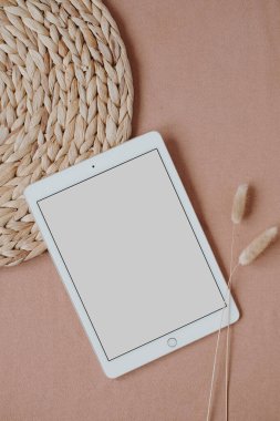 Düz tablet tablet, rattan peçete ve tavşan kuyruğu otları tarafsız pastel mercan arka planda. Estetik zarif blog, sosyal medya, web şablonu