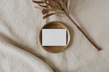 Pirinç tabakta kopya alanı olan boş bir kağıt kart nötr bej keten battaniyede kurutulmuş protea çiçeği. Üst görünüm, düz uzanan minimalist estetik lüks bohem ticari markalaşma kavramı