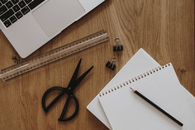Laptop, defter, kahverengi ahşap masadaki kırtasiye malzemeleri. Düz konum, üst görünüm estetik ev ofis çalışma alanı