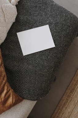 Kanepenin üzerinde battaniyeli fotokopi yeri olan boş bir kağıt kart. Üst görünüm, düz uzanan minimalist estetik lüks bohem ticari markalaşma kavramı