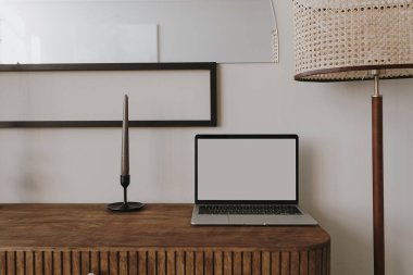 Laptop bilgisayarı ahşap konsolda, mum ve lambayla. Estetik zarif ev yapımı oturma odası iç tasarımı. Çevrimiçi mağaza, blog, sosyal medya, boş kopya alanı ile markalaşma şablonu