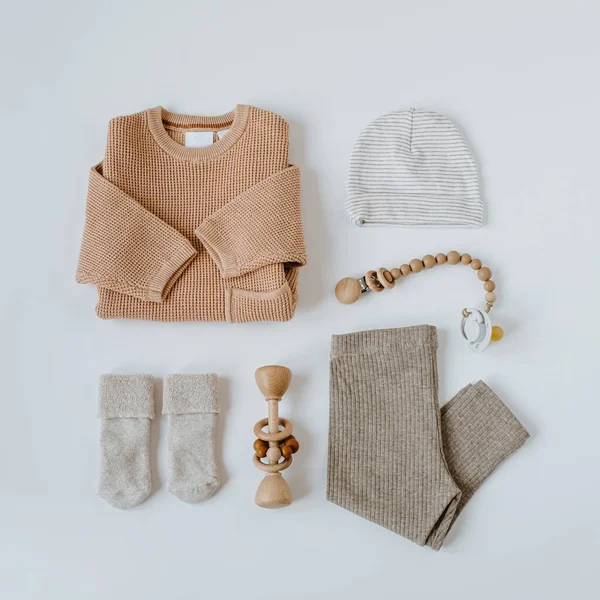 Flatlay aesthetic Scandinavian newborn baby clothes, accessories, toys collage on white background. Trendy elegant neutral pastel colour infant wear. Top view