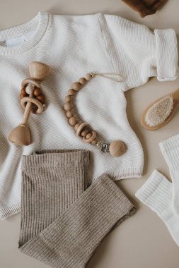 Tarafsız pastel bej arka planda zarif bebek kıyafetleri ve aksesuarlar. Süveter, tayt, emzik, fırça. Düz yatış, üst görünüm