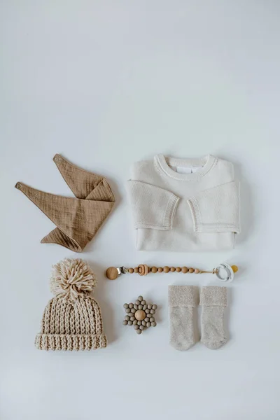 Cozy hygge pastel beige clothes and accessories for newborn baby. Warm sweater, hat, socks, muslin bib, pacifier with holder on white background. Aesthetic baby fashion collage. Flatlay