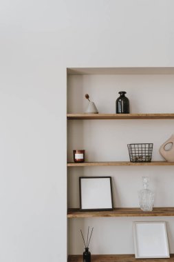 Estetik modern minimalist İskandinav ev dekorasyonu. Beyaz duvarlı zarif bohem oturma odası, mum rafları, resim çerçevesi, depolama kutusu, şişe, vazo, parfüm