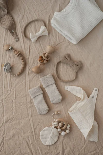 Cozy hygge pastel clothes and accessories for newborn baby. Bodysuit, socks, muslin blanket, bow, pacifier holder on neutral beige linen cloth. Aesthetic minimalist baby fashion collage