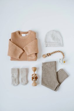 Beyaz arka planda zarif bebek kıyafetleri, aksesuarlar ve oyuncak kolajı. Şeftali rengi kazak, tozluk, önlük, emzik, şapka, çorap. Tarafsız pastel bej rengi. Düz yatış, üst görünüm