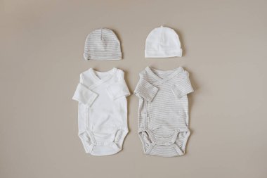 Yeni doğan bebek için rahat Hygge giysileri ve aksesuarlar. Temel kıyafetler, pastel bej arka planda şapkalar. Estetik minimalist bebek moda kolajı