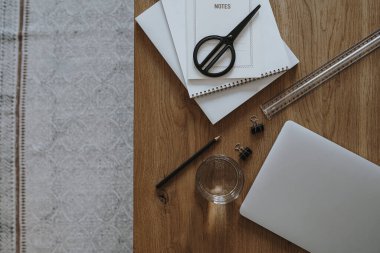 Dizüstü bilgisayar, bir bardak su, ahşap masa zemininde kırtasiye malzemesi. Düzlük, üst görünüm estetik minimal serbest yazar, blog yazarı ofis çalışma alanı.