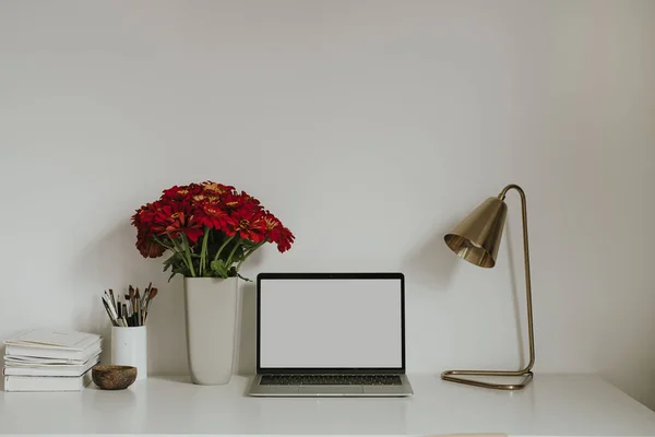 赤いガーバーの花花束とテーブルの上に空白の画面を持つノートパソコン モックアップコピースペースと審美的なインフルエンサースタイルのワークスペースのインテリアデザインテンプレート — ストック写真